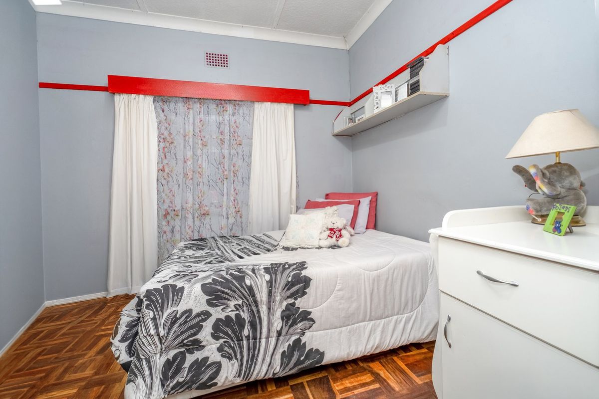 A bedroom featuring classic parquet flooring, a built-in wall shelf, and decorative red wall trim accents.