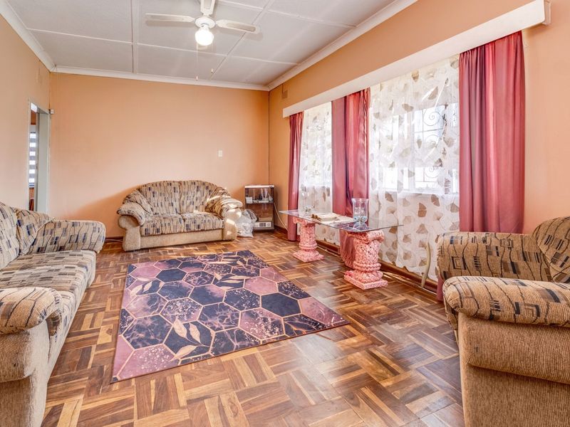 A living room featuring traditional parquet flooring, a ceiling fan, and large windows, offering a classic foundation for modern interior updates.