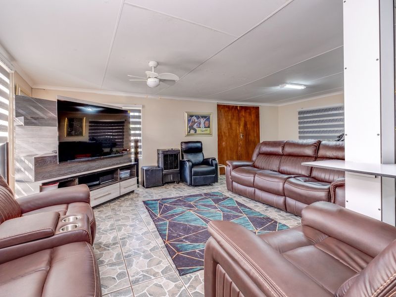 A spacious living room featuring tiled flooring, a ceiling fan, and roller blinds, providing a functional and comfortable family area.