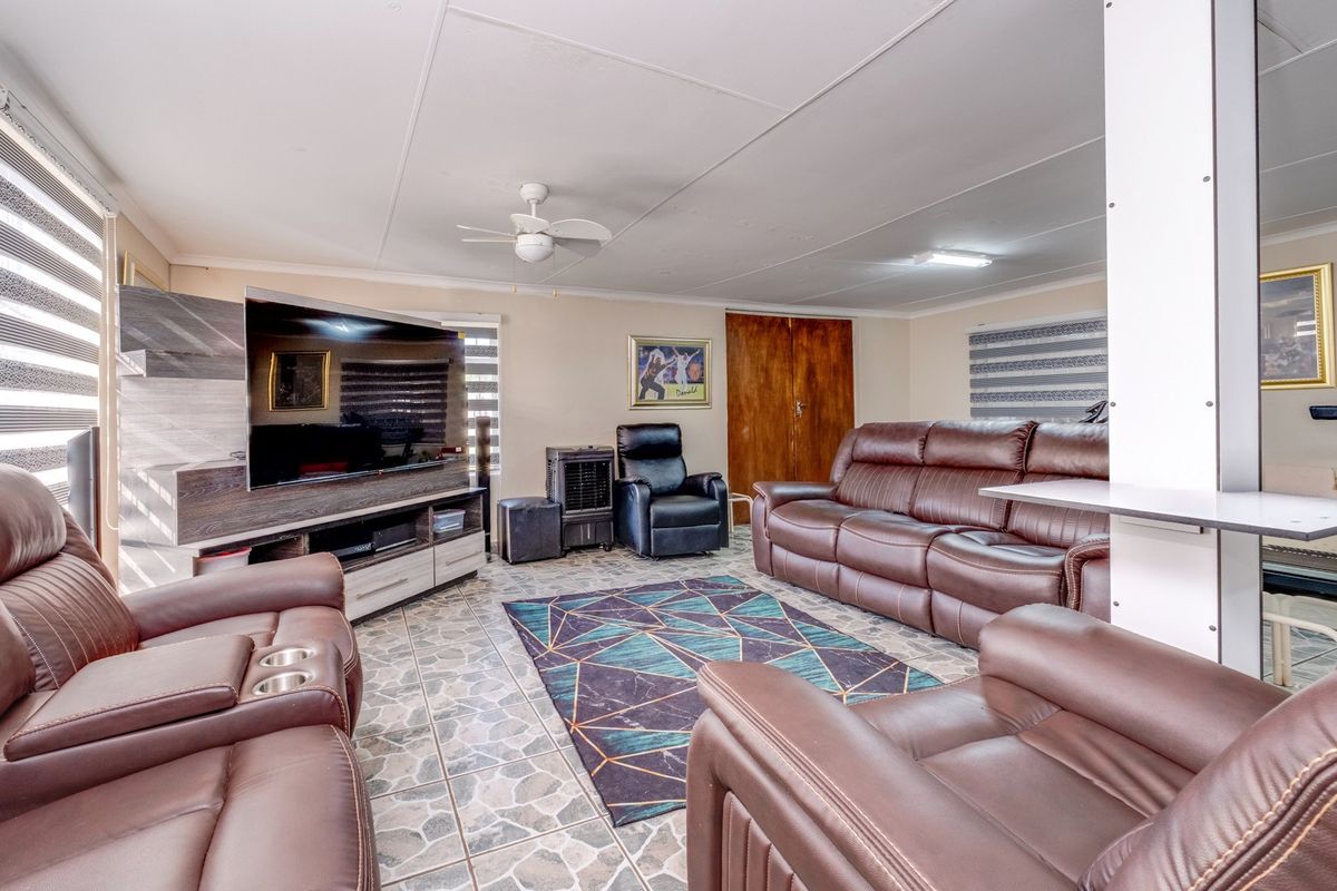 A spacious living room featuring tiled flooring, a ceiling fan, and roller blinds, providing a functional and comfortable family area.