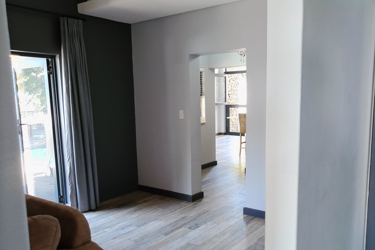 A bright living area featuring modern laminate flooring, a recessed ceiling detail, and a glass sliding door providing access to the outdoor space.
