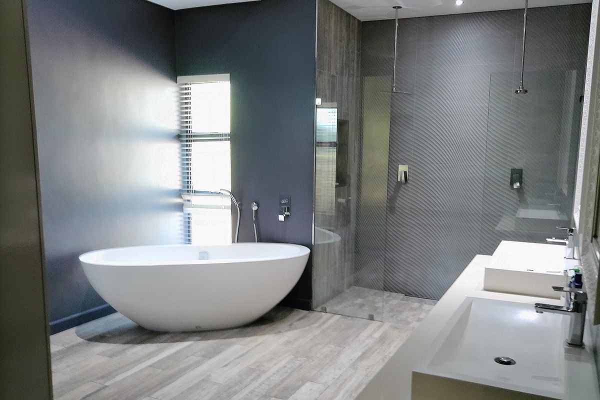 Modern bathroom featuring a sleek freestanding bathtub, a spacious walk-in shower with textured feature tiles, and a contemporary dual vanity setup.