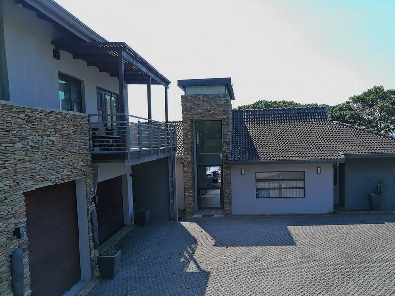 Front elevation of a modern residence featuring stone cladding, a paved driveway, double garage, and an elevated balcony with a timber pergola.