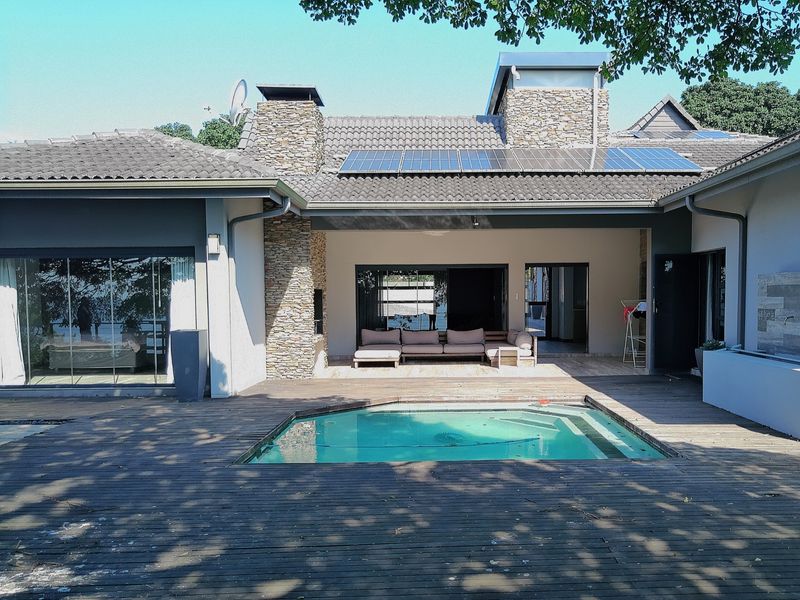 Rear exterior view featuring a swimming pool, timber decking, stone-clad chimneys, and solar panels on a tiled roof with integrated patio space.