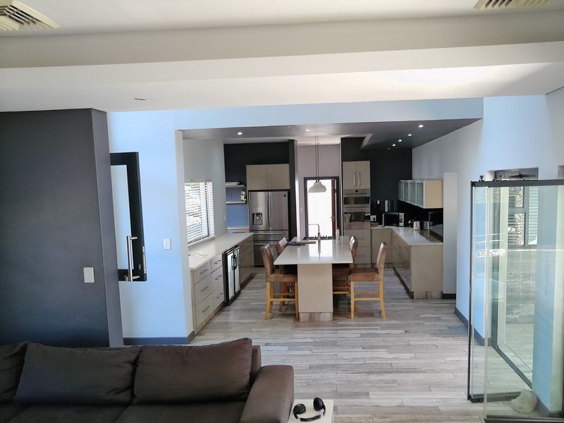 Spacious open-plan kitchen featuring a central island, modern cabinetry, integrated appliances, and sleek tiled flooring, seamlessly connecting to the living area.