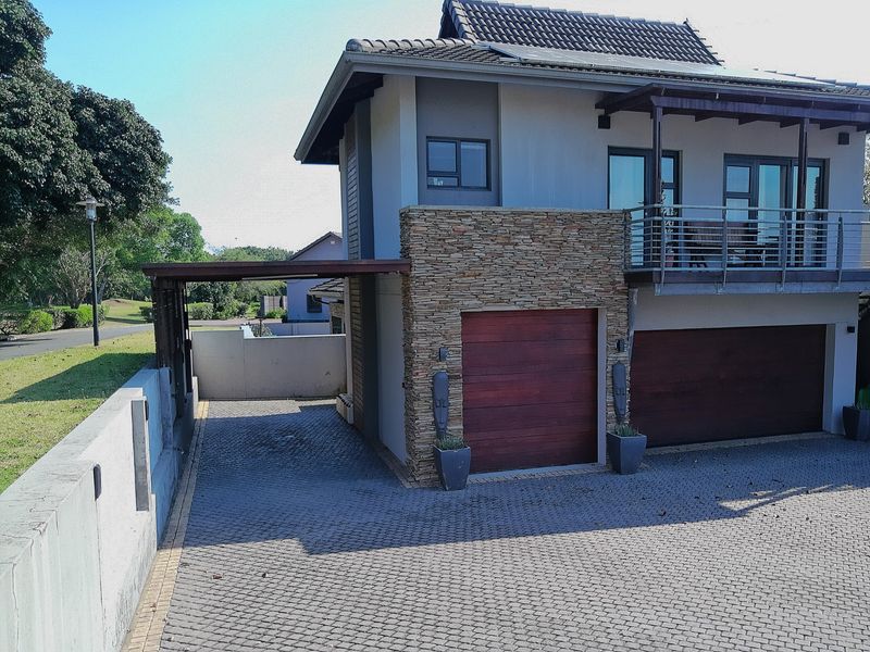 Front elevation of a modern double-storey house featuring a double garage, stone cladding accents, a paved driveway, and an upper-level balcony.