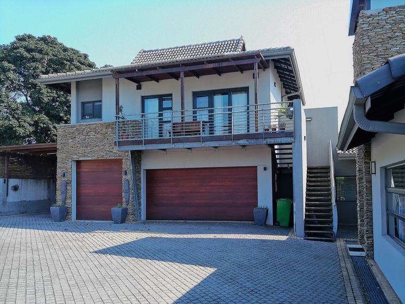 Front elevation of a multi-level home featuring a double and single garage, stone cladding accents, and an upper-level balcony with a timber pergola.