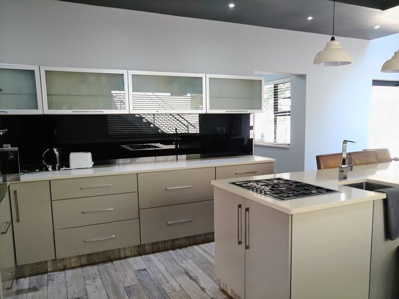 Modern kitchen featuring a central island with a gas hob, stone countertops, sleek cabinetry, and contemporary pendant lighting.