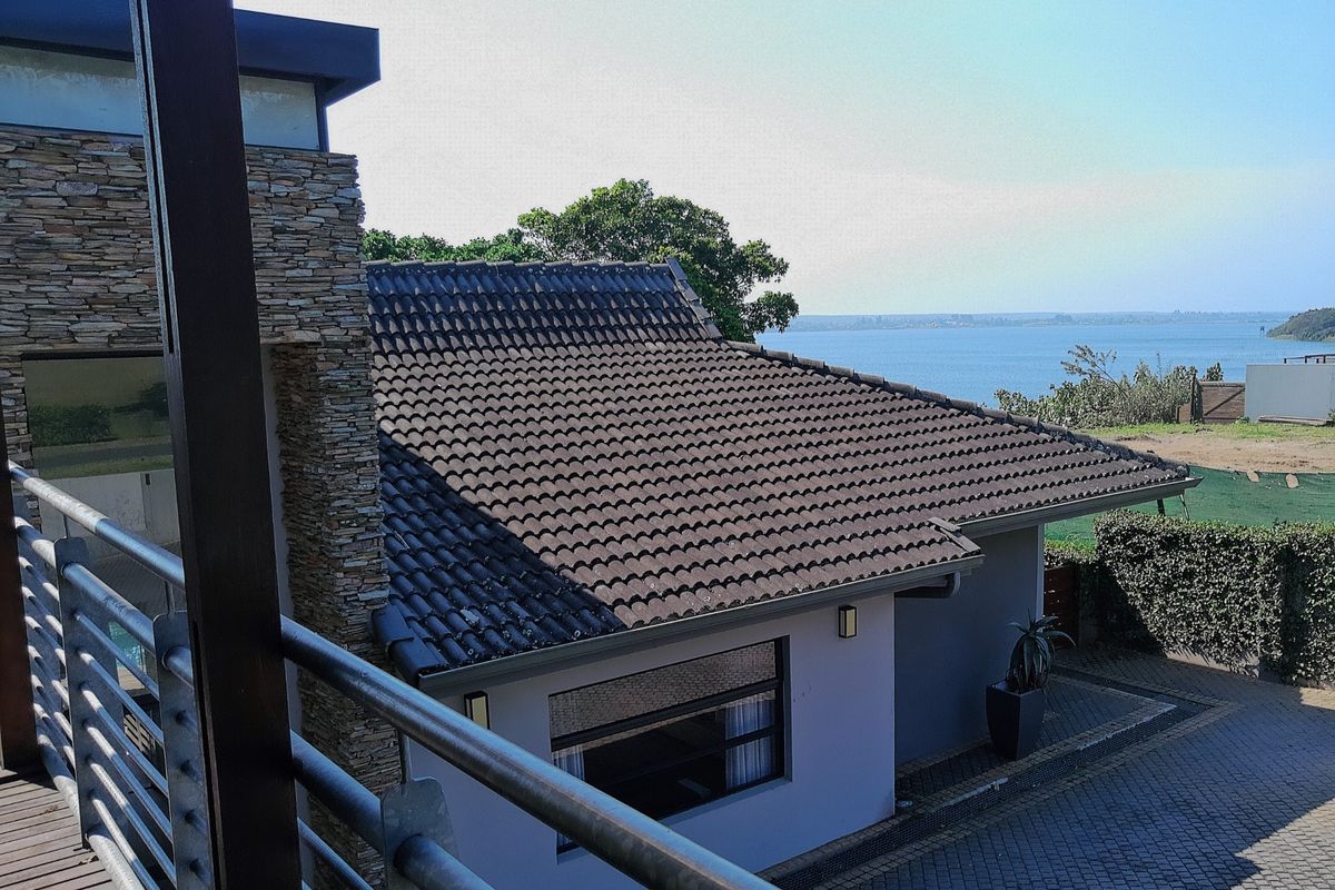 Elevated view of the rear exterior featuring a tiled roof, stone cladding, paved driveway, and a balcony overlooking the water.