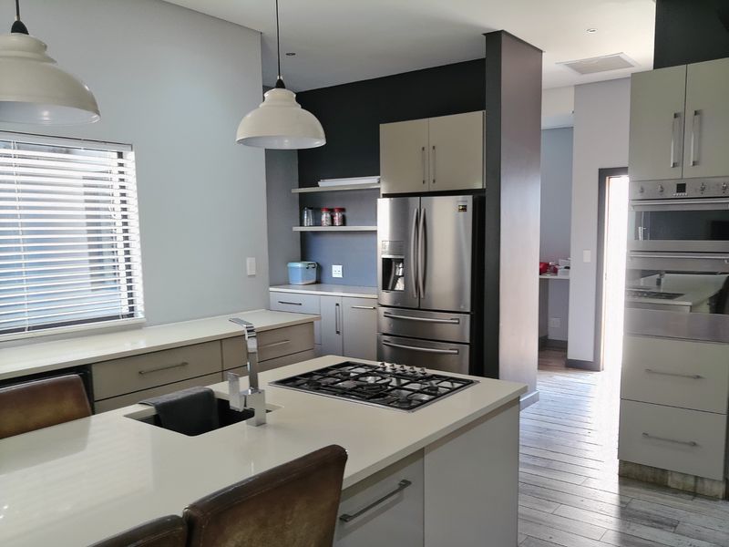 Modern kitchen featuring a central island with a gas hob, integrated appliances, sleek cabinetry, and contemporary pendant lighting.