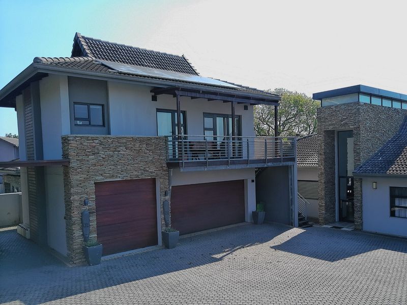Modern double-story residence featuring stone cladding, a double garage, a private balcony, and a paved driveway with integrated solar panels on the roof.