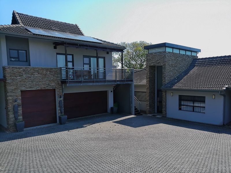 Modern double-story residence featuring stone cladding, a spacious paved driveway, integrated double garage, and an upper-level balcony with solar panel installation.