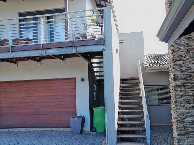 Front exterior view featuring a garage, an elevated balcony with metal railings, and an external staircase leading to the upper level.