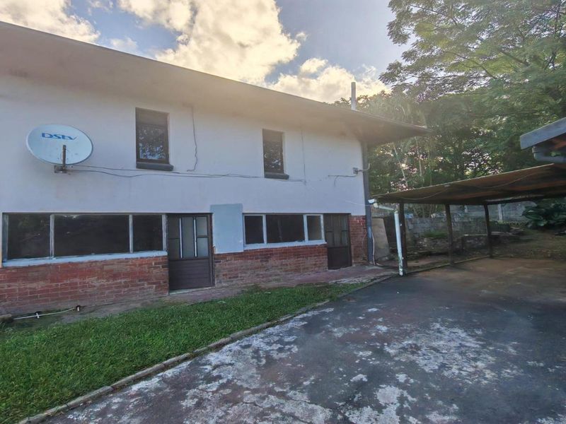 Rear exterior view of the house featuring a brick and plaster facade, a covered carport, and a concrete driveway area.