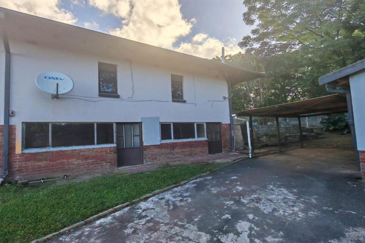 Rear exterior view of the house featuring a brick and plaster facade, a covered carport, and a concrete driveway area.