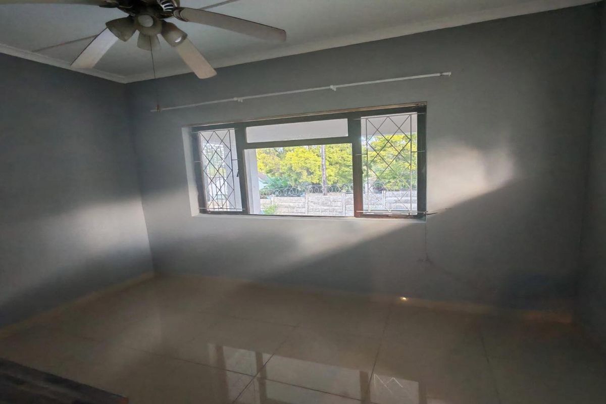 An empty bedroom featuring tiled flooring, a ceiling fan, and security bars on the window.