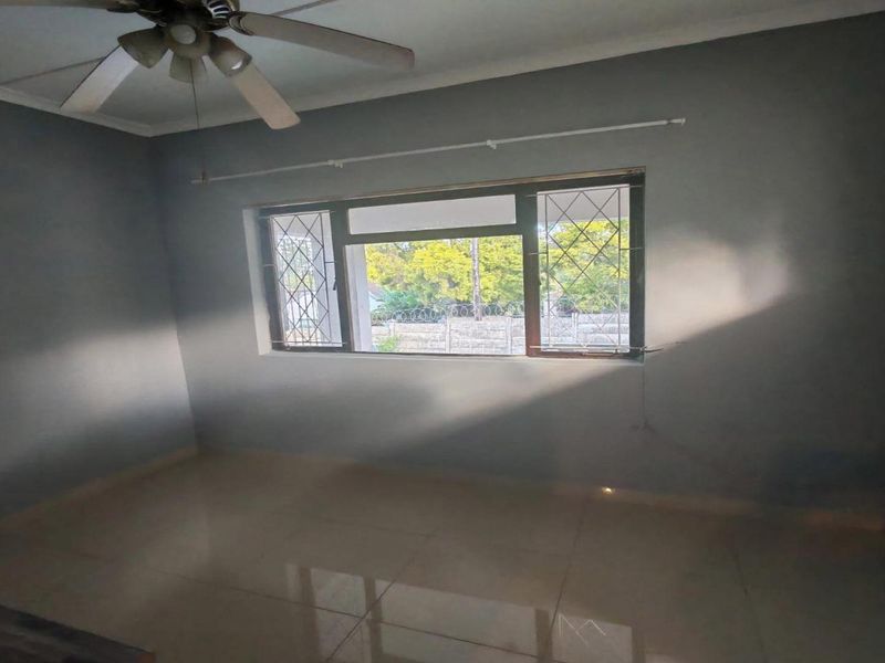 An empty bedroom featuring tiled flooring, a ceiling fan, and security bars on the window.
