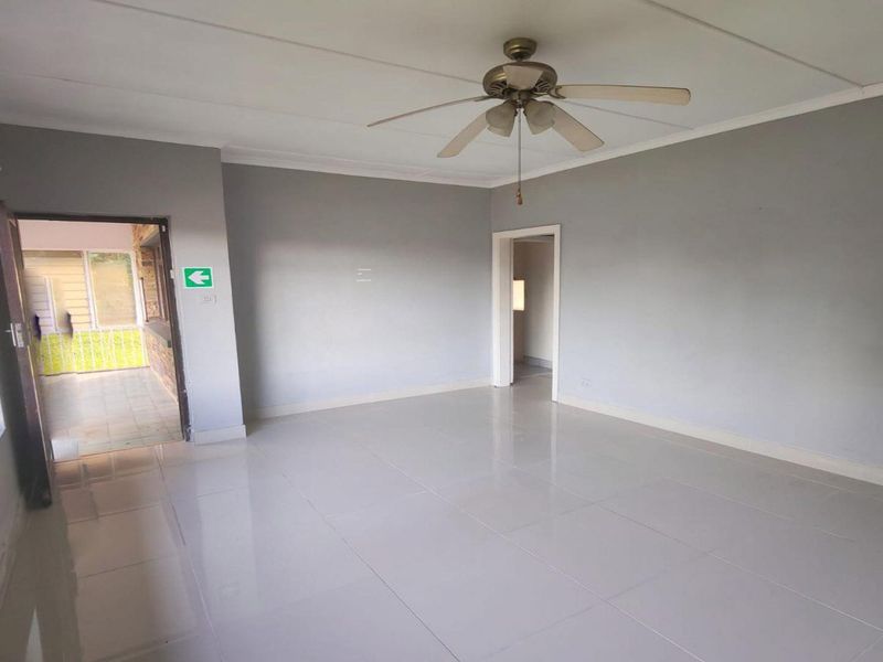 A spacious, empty living area featuring neutral grey walls, polished tiled flooring, and a ceiling fan, with direct access to an outdoor patio.