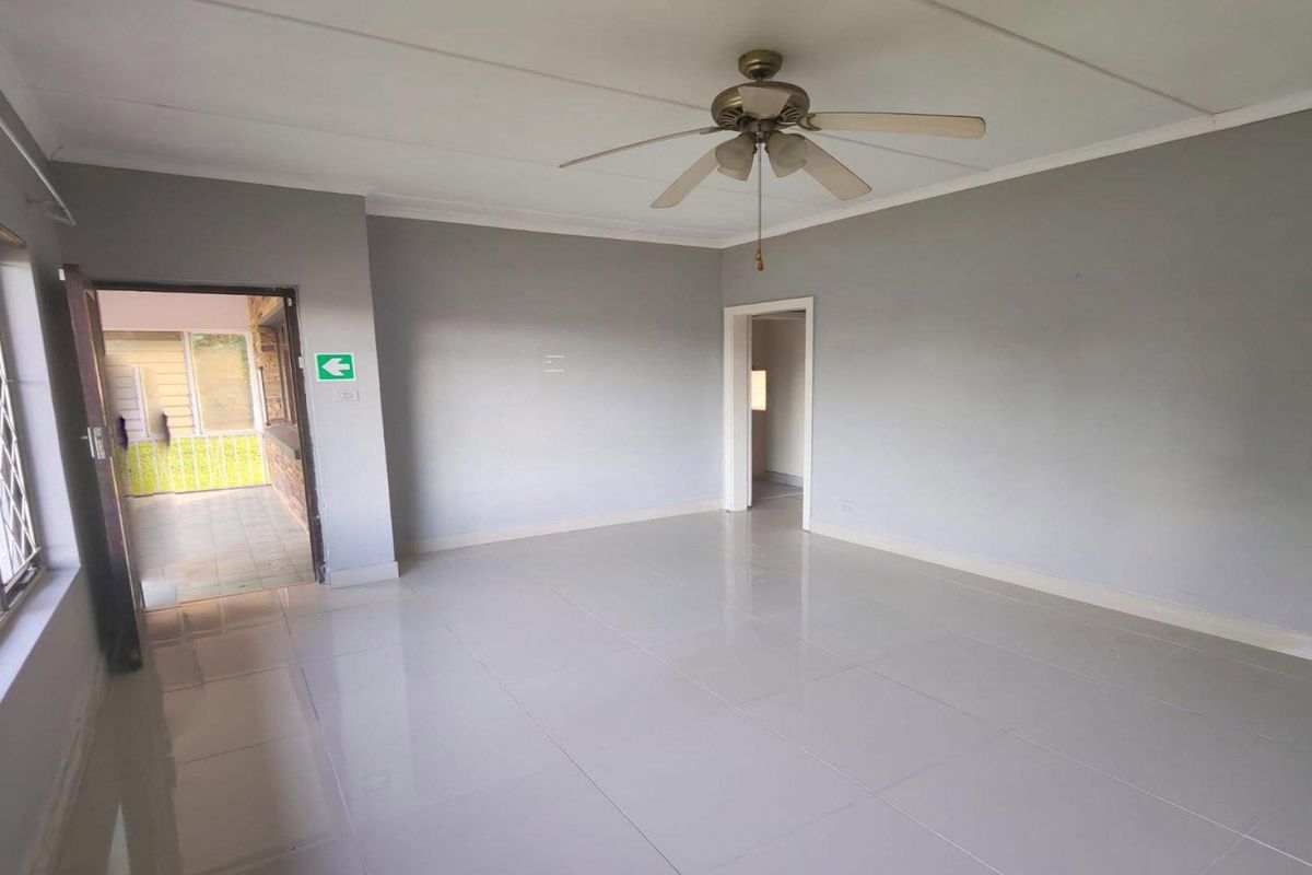 A spacious, empty living area featuring neutral grey walls, polished tiled flooring, and a ceiling fan, with direct access to an outdoor patio.