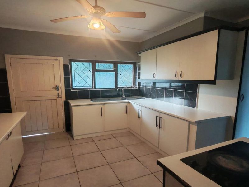 A functional kitchen featuring white built-in cabinetry, tiled flooring, a tiled backsplash, and a ceiling fan, offering a clean and practical workspace.