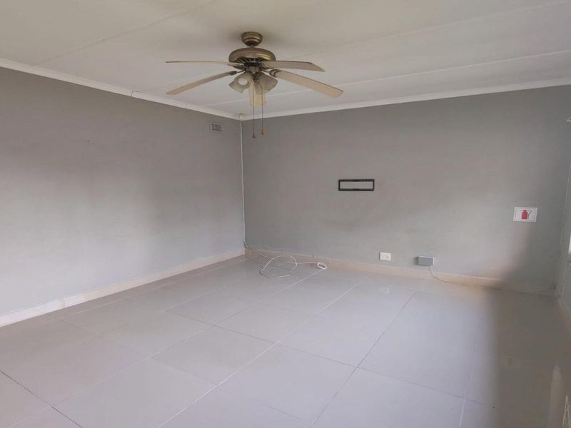 A spacious, empty living room featuring neutral grey walls, tiled flooring, and a ceiling fan, offering a blank canvas for interior design.