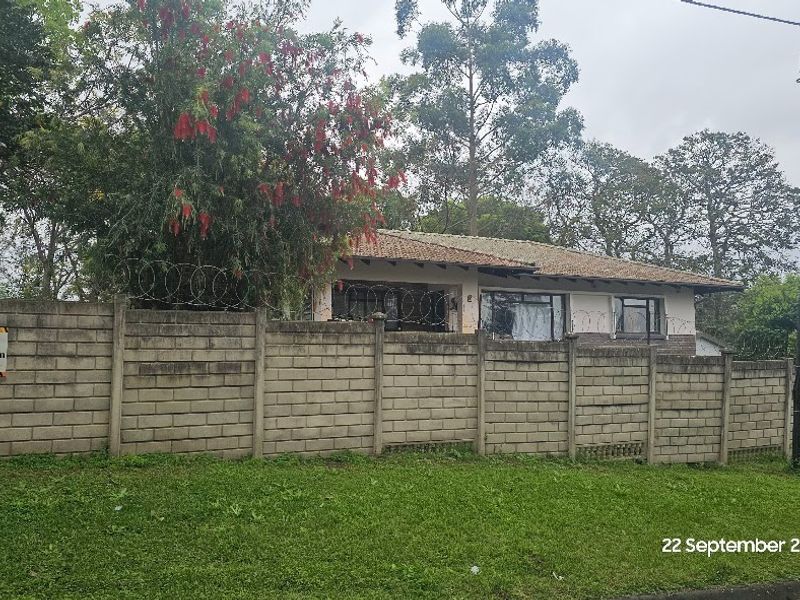 Front view of a residential property featuring a concrete block boundary wall with security razor wire and a tiled roof structure.