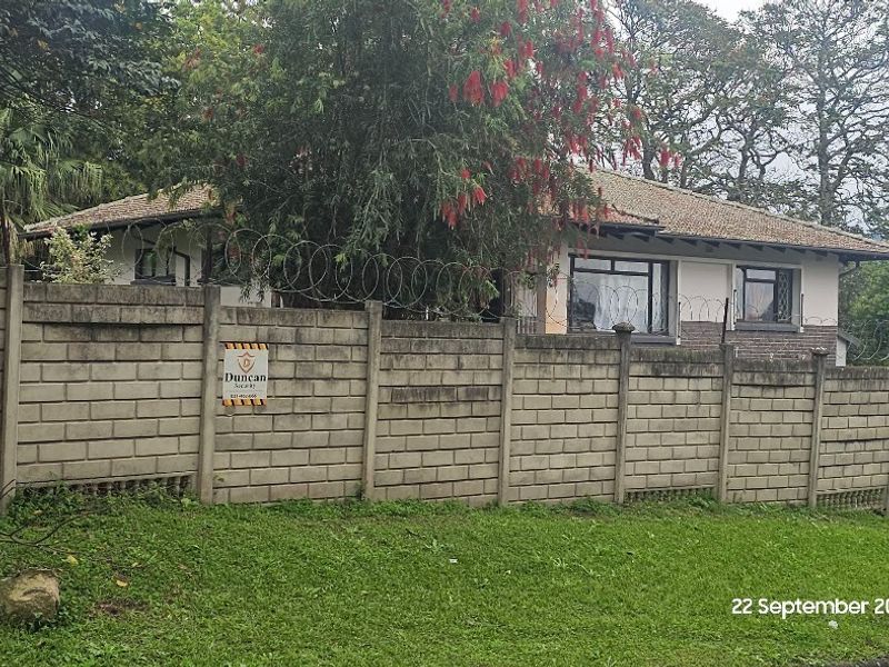 Front view of a residential property featuring a concrete block boundary wall with security razor wire and a tiled roof structure.
