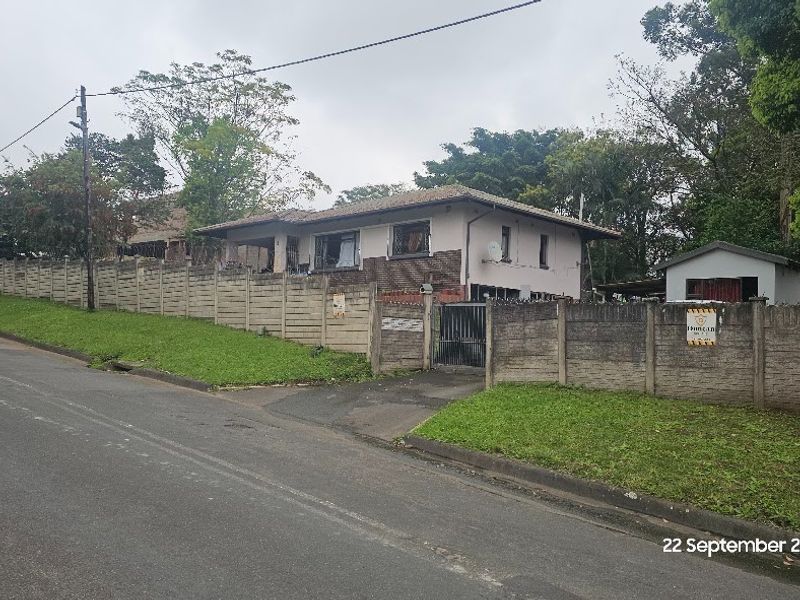 Street view of a residential property featuring a precast concrete boundary wall, metal driveway gate, and a detached garage structure.