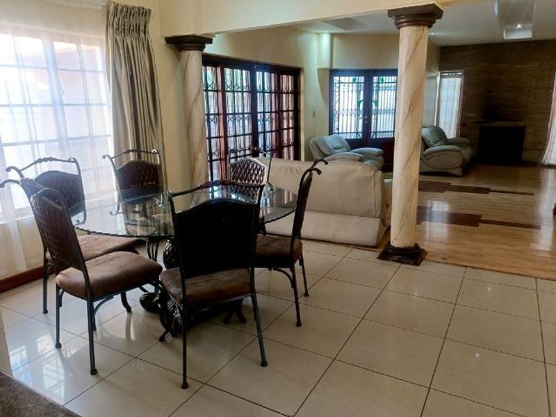 Spacious open-plan living and dining area featuring a mix of tiled and hardwood flooring, decorative columns, and large sliding doors leading outdoors.