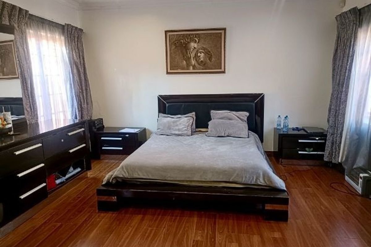 A spacious bedroom featuring warm-toned laminate flooring, decorative cove cornicing, and recessed ceiling lighting, providing a comfortable and functional sleeping area.