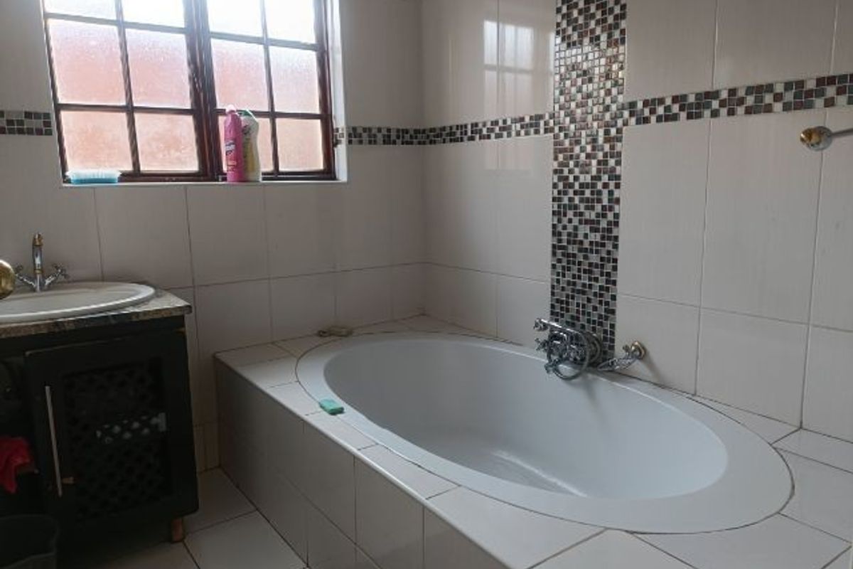 A functional bathroom featuring a built-in oval bathtub, a vanity cabinet with a basin, and decorative mosaic tile accents on the wall.