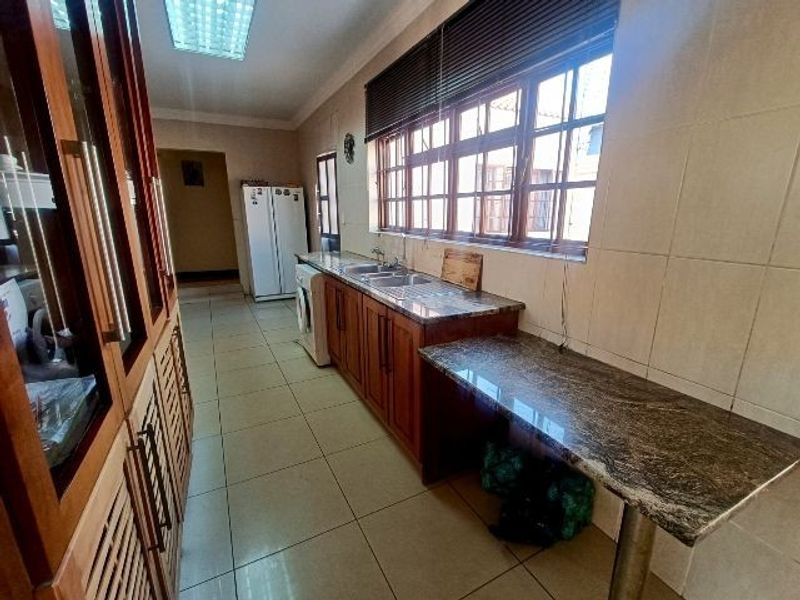 A functional kitchen featuring wooden cabinetry, granite countertops, a double basin sink, and tiled flooring with ample natural light.