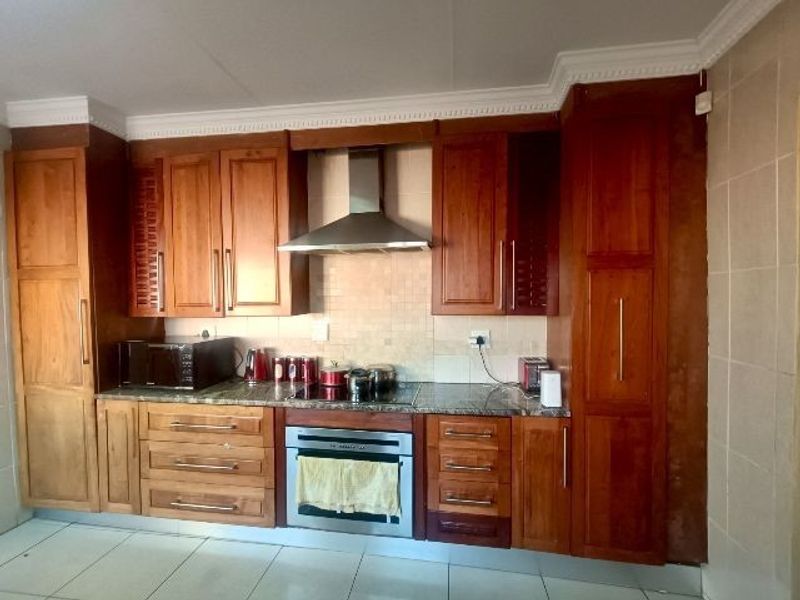 A functional kitchen featuring warm-toned wooden cabinetry, granite countertops, a built-in oven with a stainless steel extractor fan, and tiled flooring.