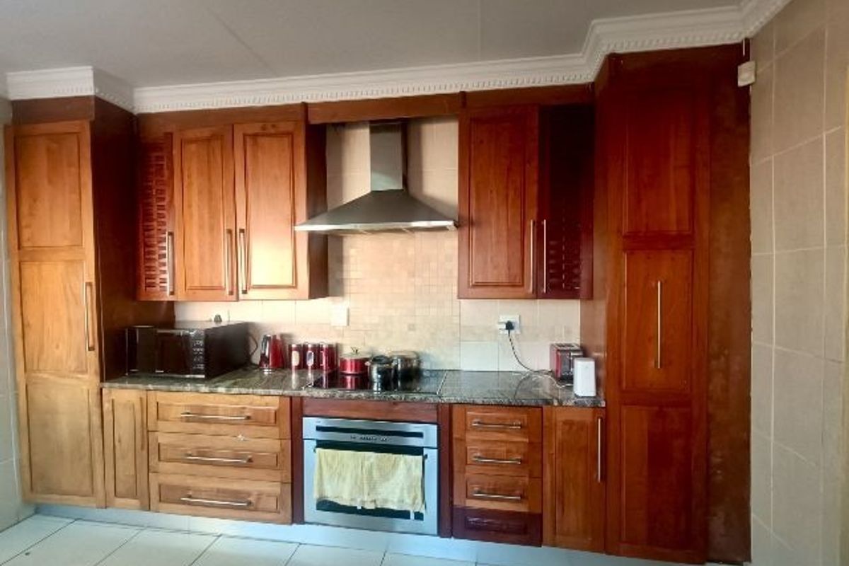 A functional kitchen featuring warm-toned wooden cabinetry, granite countertops, a built-in oven with a stainless steel extractor fan, and tiled flooring.
