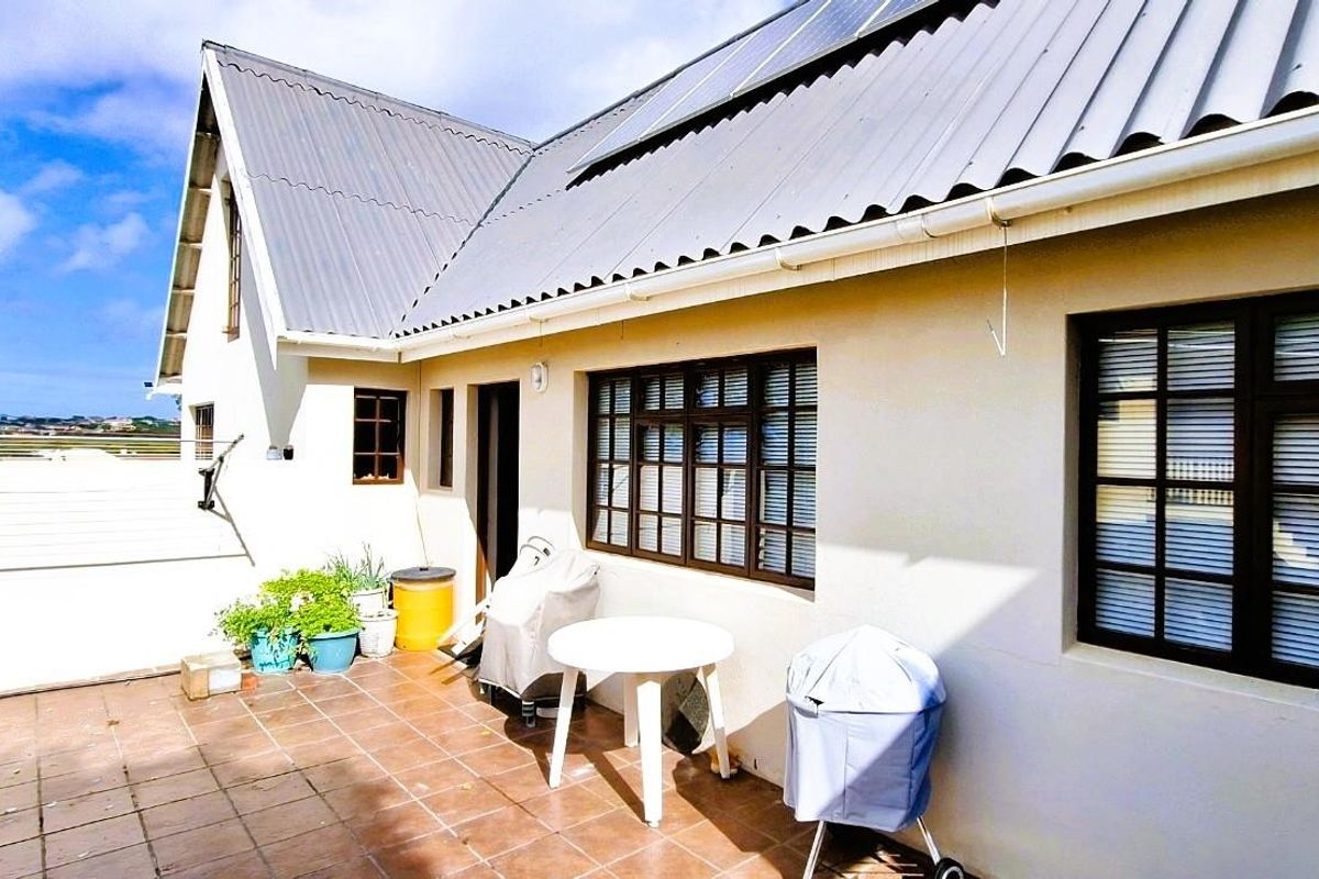 Rear exterior view of the house featuring a tiled patio area, corrugated metal roofing, and installed solar panels.