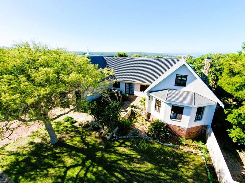 An elevated aerial view of a well-maintained residential property featuring a metal roof, stone chimney, and established garden landscaping.
