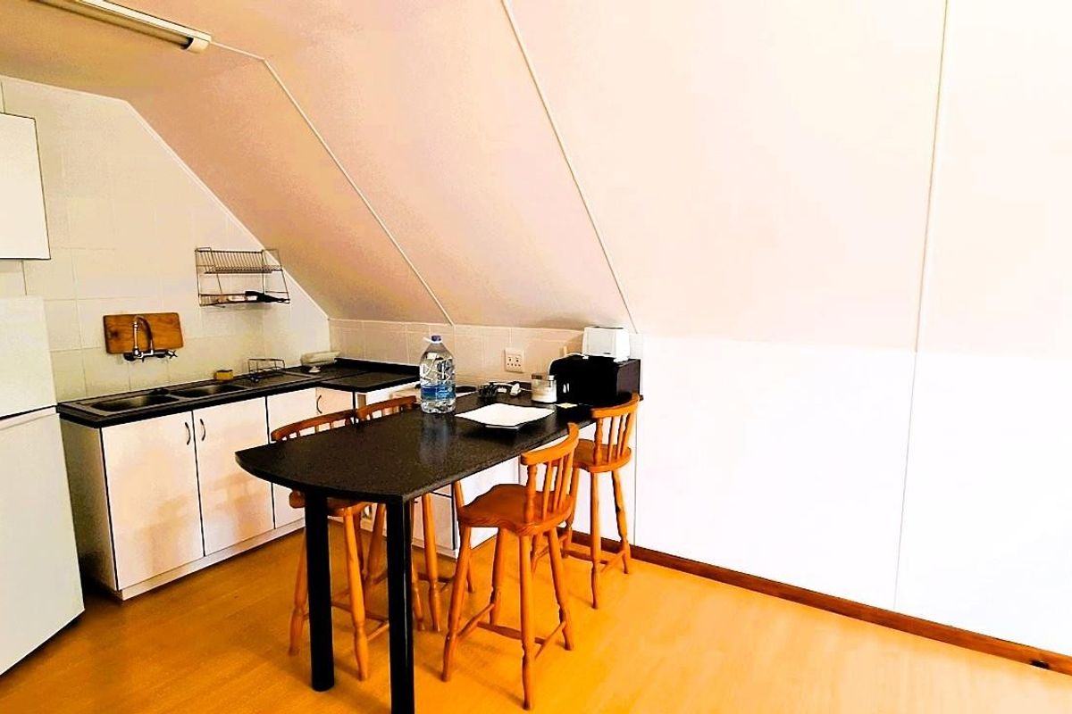 Compact kitchen area featuring built-in cabinetry, laminate countertops, and a tiled splashback, situated under a sloped ceiling.