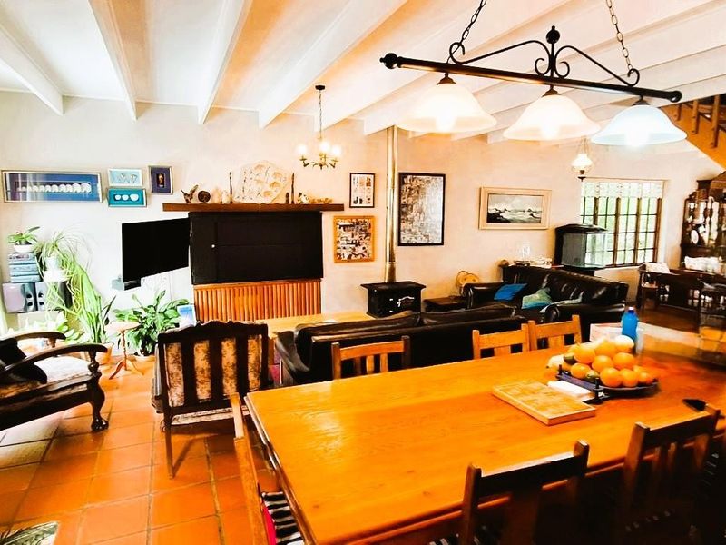 Spacious open-plan living and dining area featuring exposed beam ceilings, terracotta flooring, a wood-burning stove, and an integrated kitchen space.