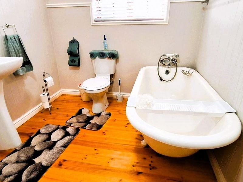 A bathroom featuring a classic clawfoot bathtub, pedestal basin, and toilet, finished with timber flooring and wall paneling.