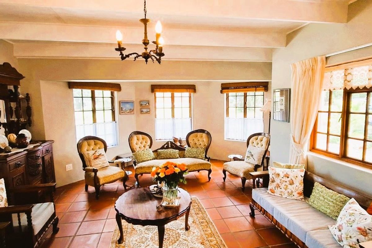 A spacious living room featuring exposed ceiling beams, terracotta floor tiles, and large timber-framed windows that provide ample natural light.