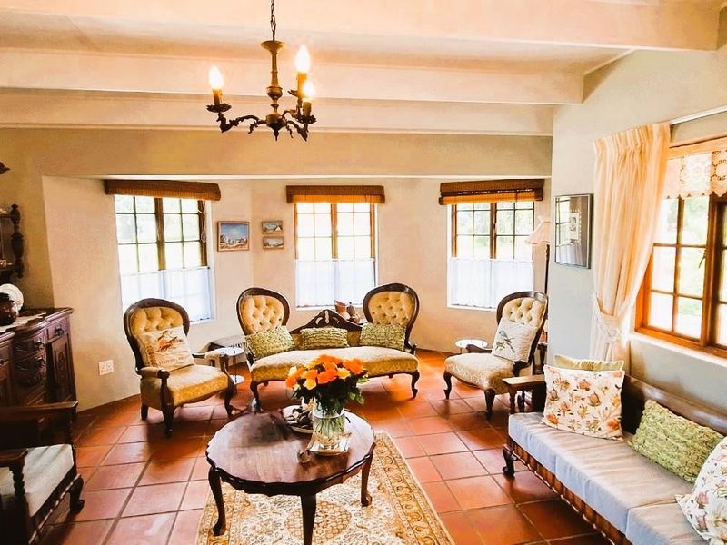 A spacious living room featuring exposed ceiling beams, terracotta floor tiles, and large timber-framed windows that provide ample natural light.