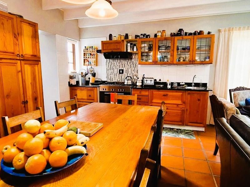 Open-plan kitchen and dining area featuring warm wooden cabinetry, tiled flooring, exposed ceiling beams, and a functional gas stove setup.