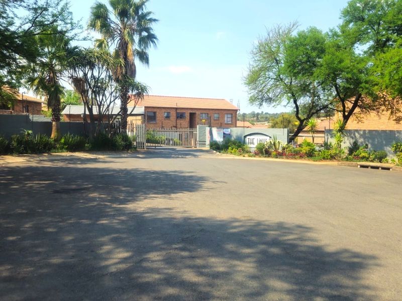 Street view of the apartment complex entrance featuring a paved driveway, perimeter wall, and security gate access.