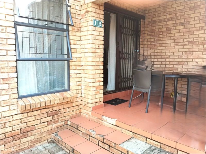 Front entrance of apartment 115 featuring face brick exterior, security gate, and tiled steps with visible damage to the tile edges.