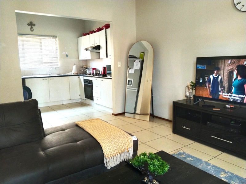 Open plan living area featuring a functional kitchen with built-in cabinetry, oven, and hob, seamlessly flowing into the lounge space with tiled flooring throughout.