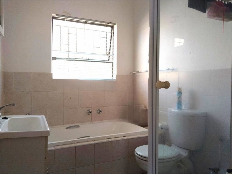 A functional bathroom featuring a built-in bathtub, shower enclosure, toilet, and vanity basin with tiled walls and security-barred window.