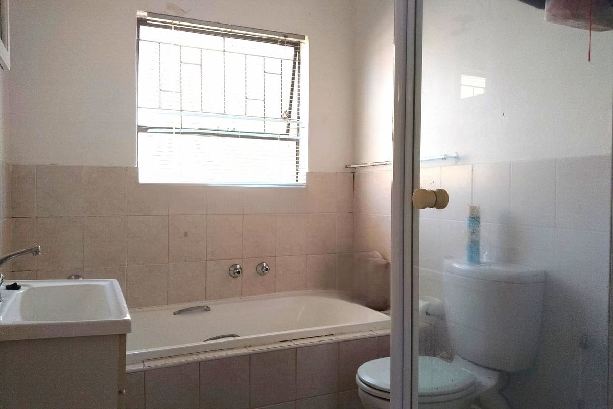 A functional bathroom featuring a built-in bathtub, shower enclosure, toilet, and vanity basin with tiled walls and security-barred window.