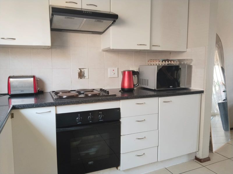A functional kitchen featuring white cabinetry, a dark laminate countertop, built-in oven, electric hob, and an extractor fan with a tiled backsplash.