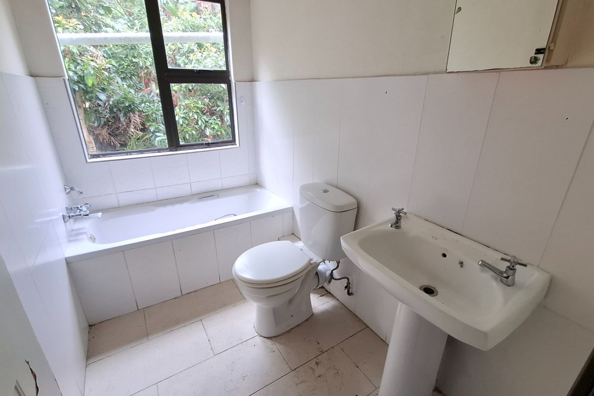 A dated bathroom featuring a standard bathtub, pedestal basin, and toilet with tiled finishes, requiring cosmetic updates to modernize the space.