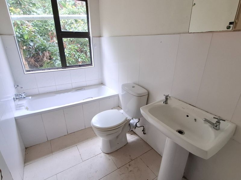 A dated bathroom featuring a standard bathtub, pedestal basin, and toilet with tiled finishes, requiring cosmetic updates to modernize the space.